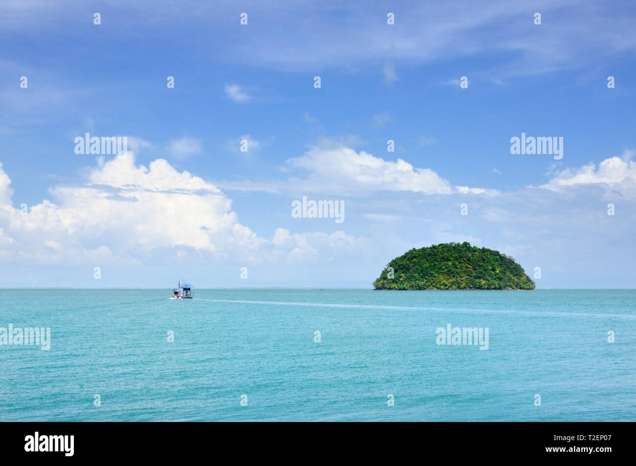 Turquoise tropical sea with fishing boat and small island on horizon under blue sky with scenic clouds at the Koh Chang island, Thailand. Stock Photo