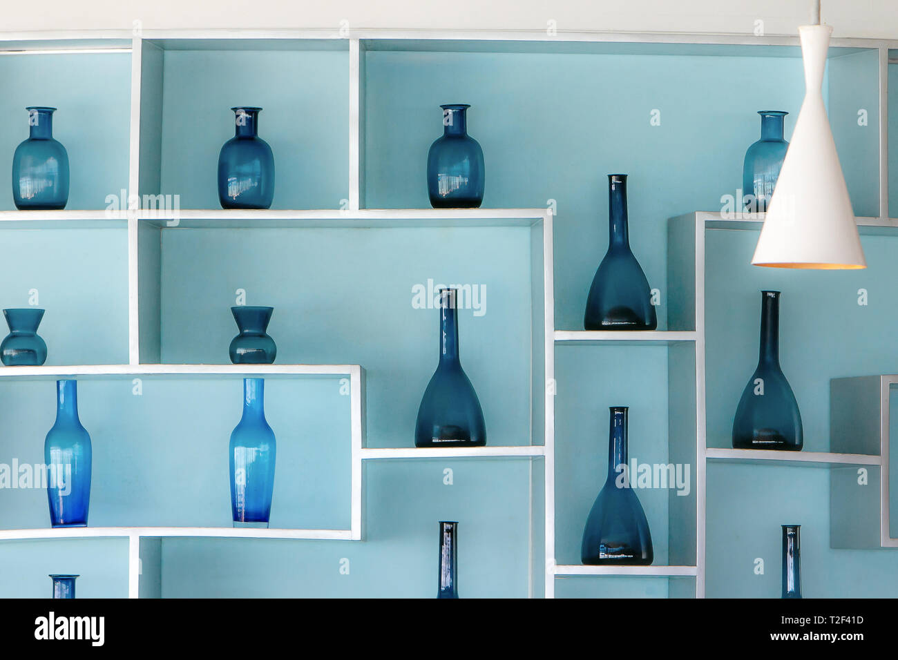 Retro style blue glass bottles in a beautiful arrangement on shelves attached to a light blue wall. Stock Photo