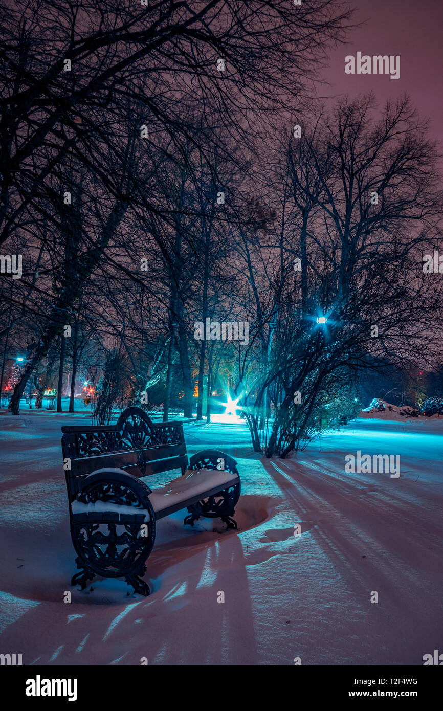 Winter scene with a bench in the park in the night covered in snow close to a street lamp in Bucharest Stock Photo