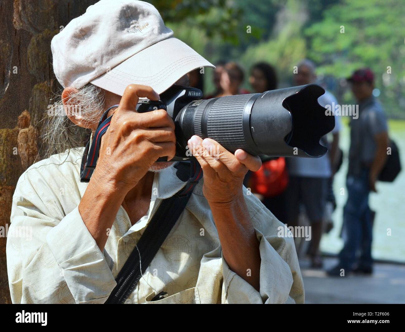 Elderly Vietnamese street photographer takes candid photos with his Nikon DSLR camera with a telephoto lens. Stock Photo