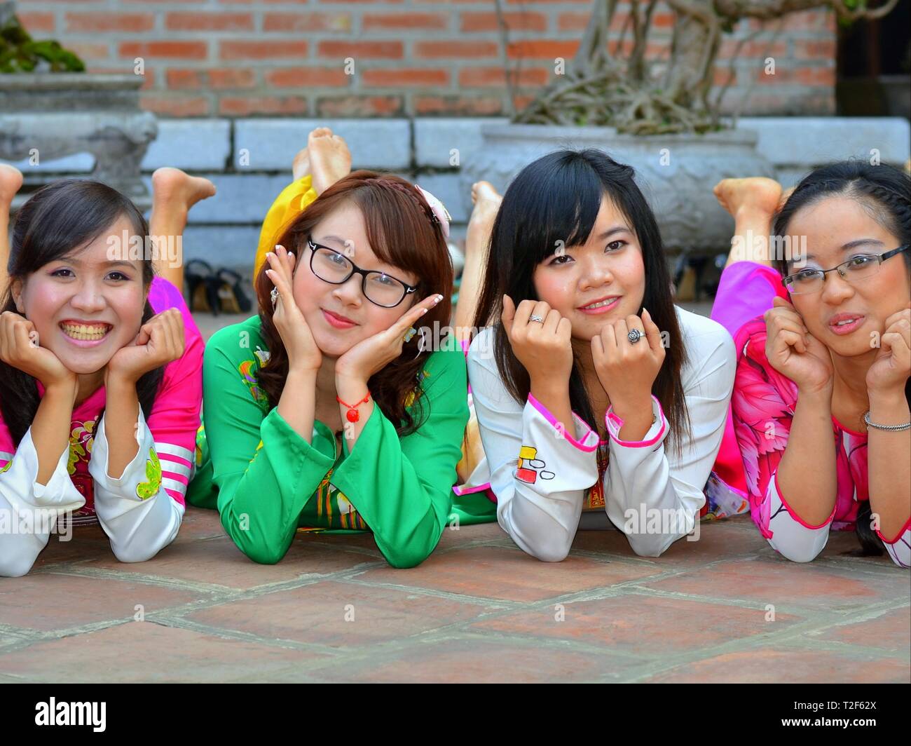 Four dressed-up Vietnamese girls in a prone position rest their heads on their hands and look at the camera. Stock Photo