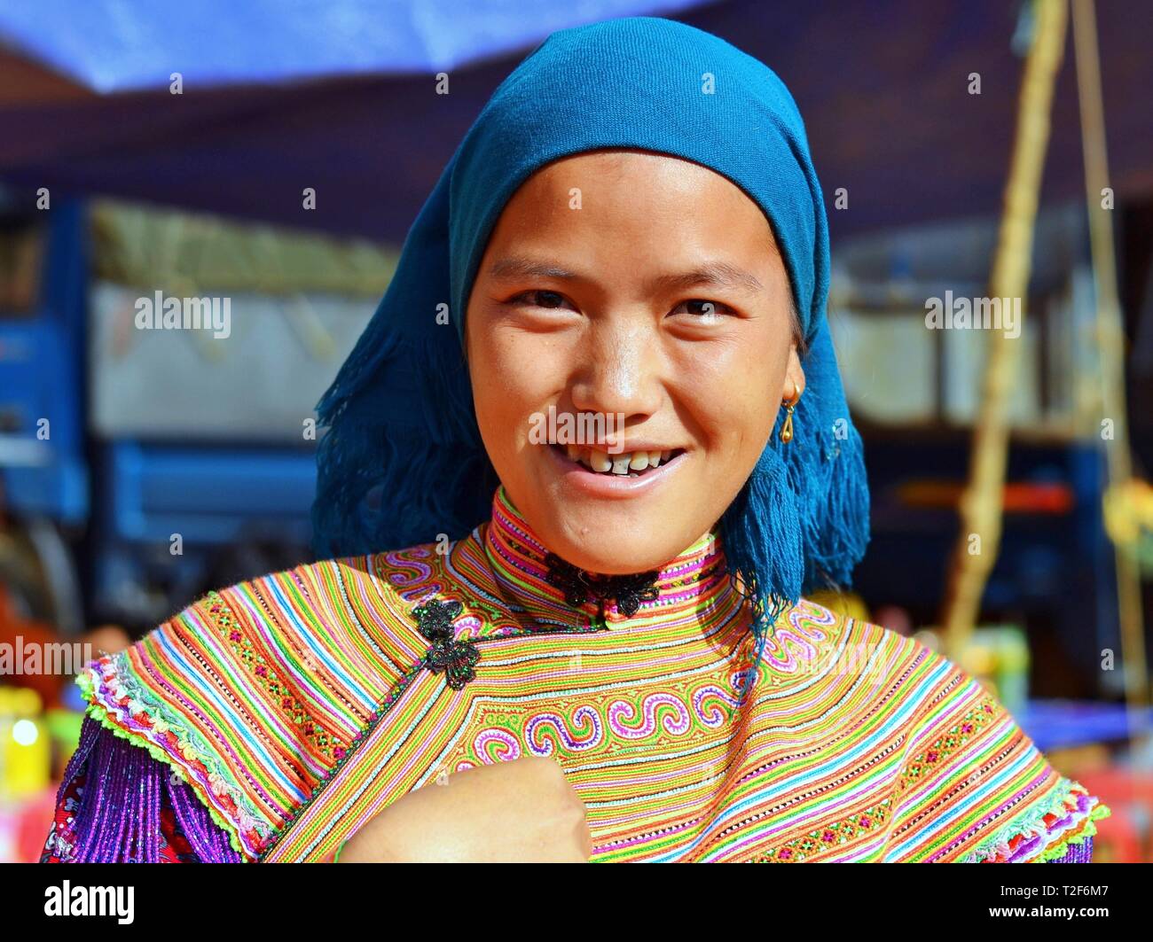 Young Vietnamese Flower H'mong woman wearsa colourful traditional Flower H'mong attire and a blue headscarf and smiles for the camera. Stock Photo