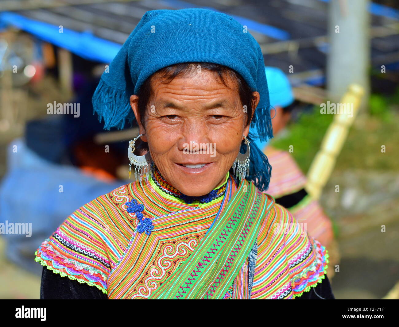 Elderly Vietnamese Flower H'mong woman wears the traditional costume of the Flower H'mong people, a blue headscarf and large silver earrings. Stock Photo