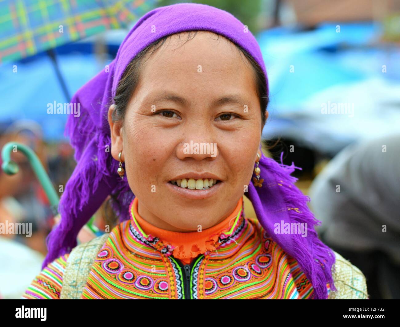 Mature Vietnamese Flower H'mong woman wears the colourful traditional costume of the Flower H'mong people, a blue headscarf and small earrings. Stock Photo