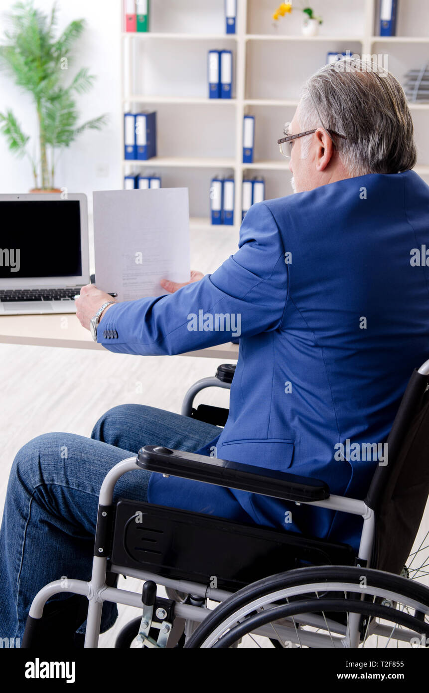 Aged employee in wheelchair working in the office Stock Photo