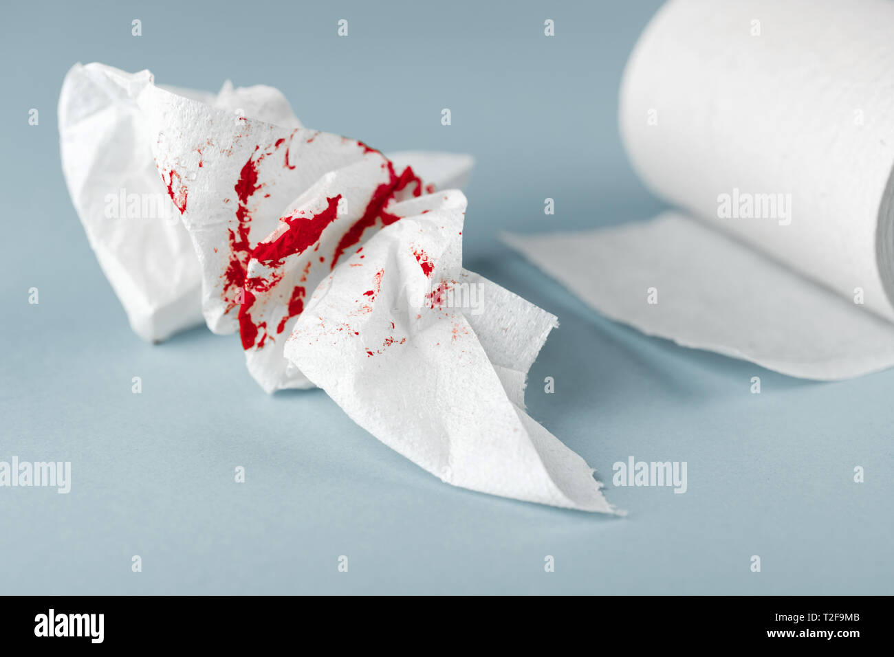 A photo of used bloody toilet paper and a toilet paper roll on the light blue background. Menstrual or hemorrhoids bleeding Stock Photo