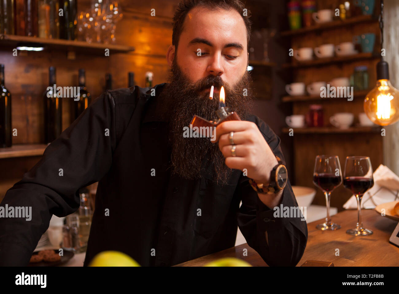 Bearded handsome young bartender lighting his cigarette in vintage pub