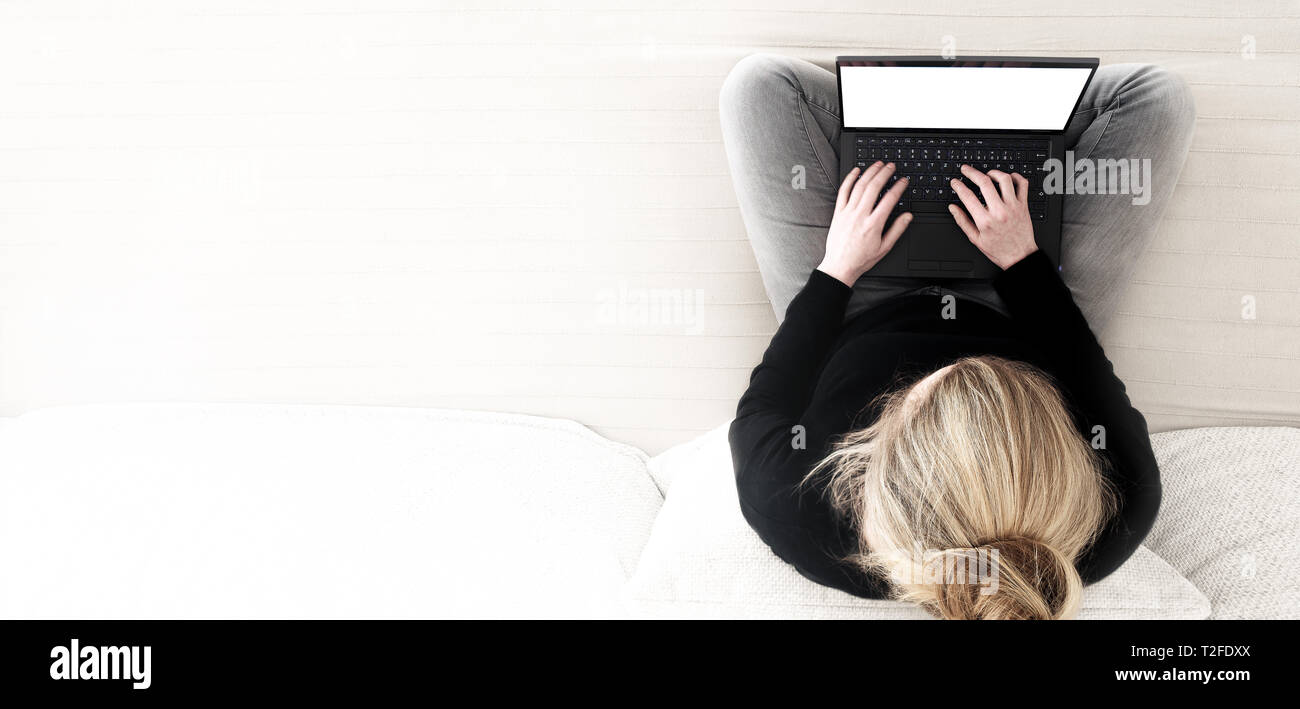 directly above shot of young blonde caucasian woman cross-legged sitting on sofa working on laptop computer Stock Photo