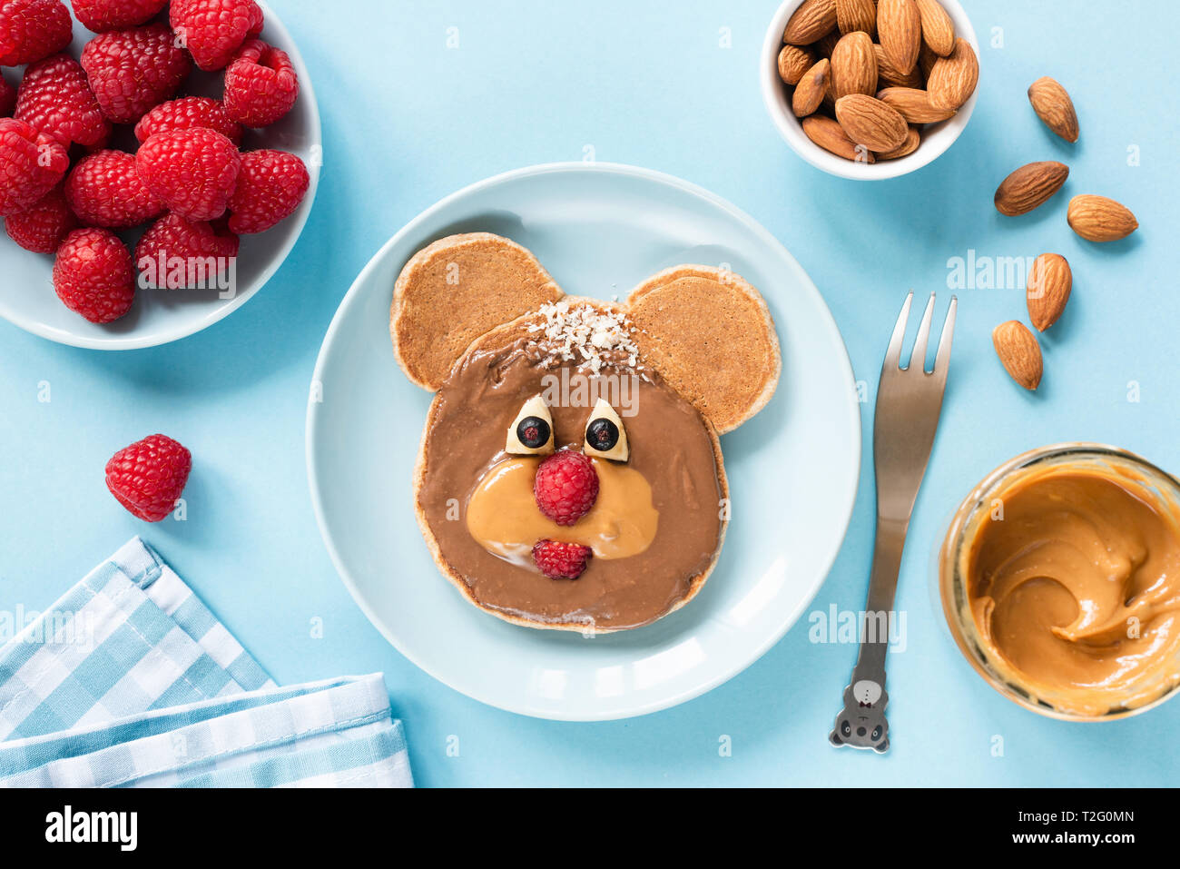 Cute funny pancake food art for kids. Bear or dog shaped pancake with peanut butter and berries. Blue background. Healthy colorful children breakfast Stock Photo