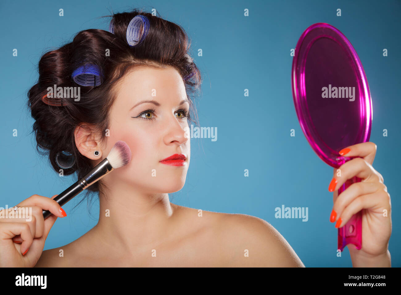 Cosmetic Beauty Procedures And Makeover Concept Woman In Hair Curlers Applying Makeup Blusher With Brush Girl Gets Blush On Cheekbones On Blue Stock Photo Alamy