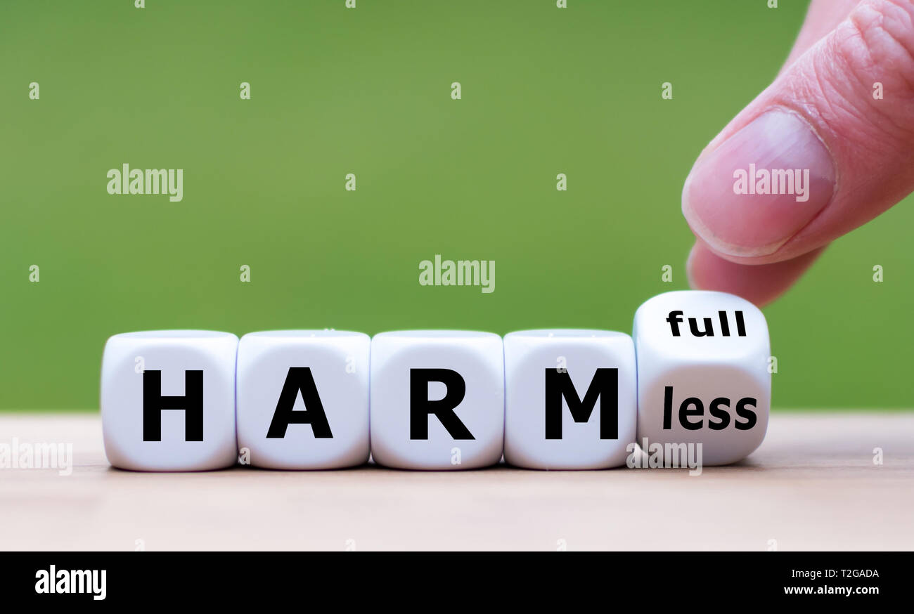 Hand turns a dice and changes the expression 'harmful' to 'harmless'. Stock Photo