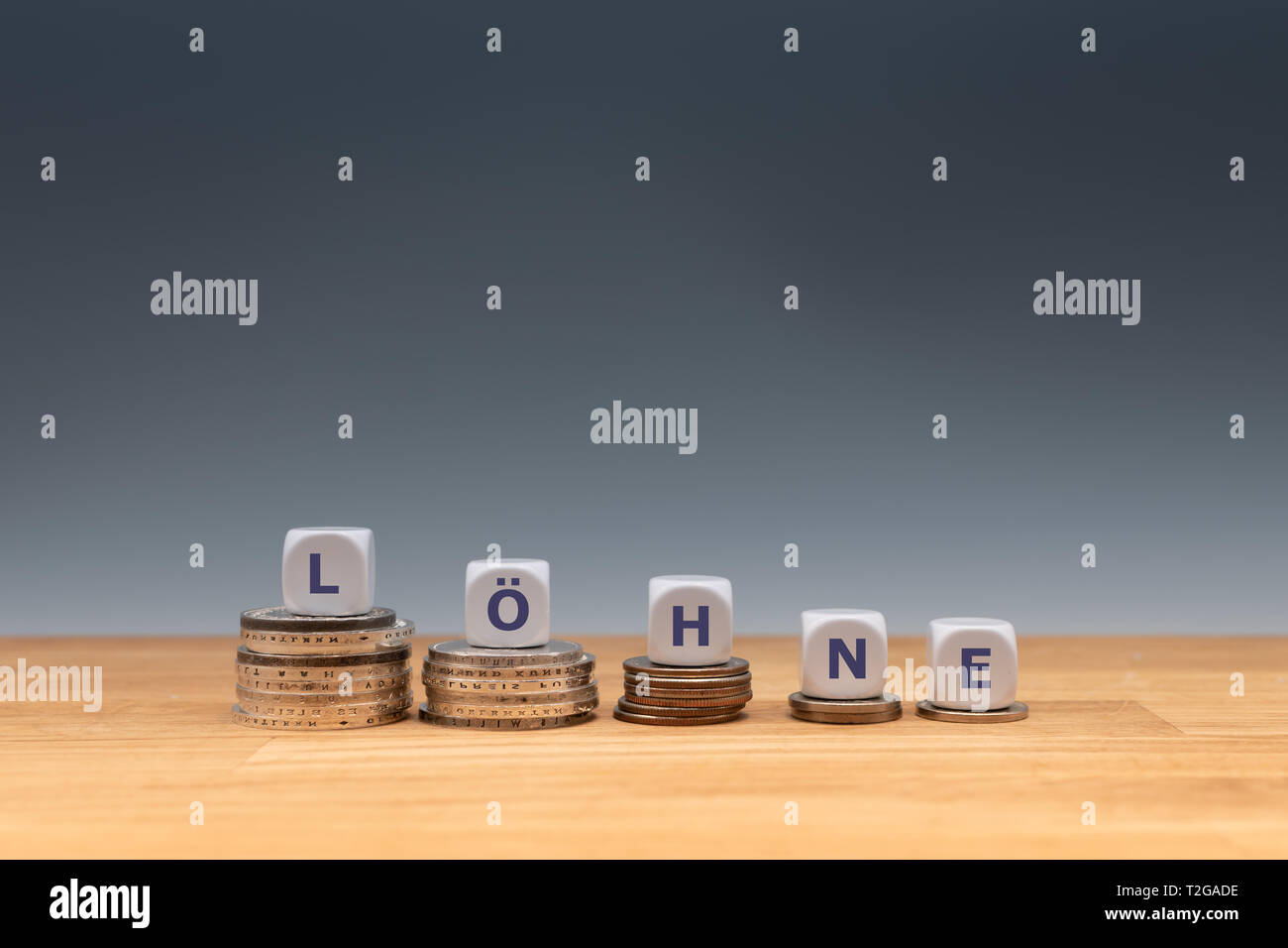 Symbol for declining wages. Dice placed on stacks of coins form the German word 'LÖHNE' ('WAGES' in English). Stock Photo