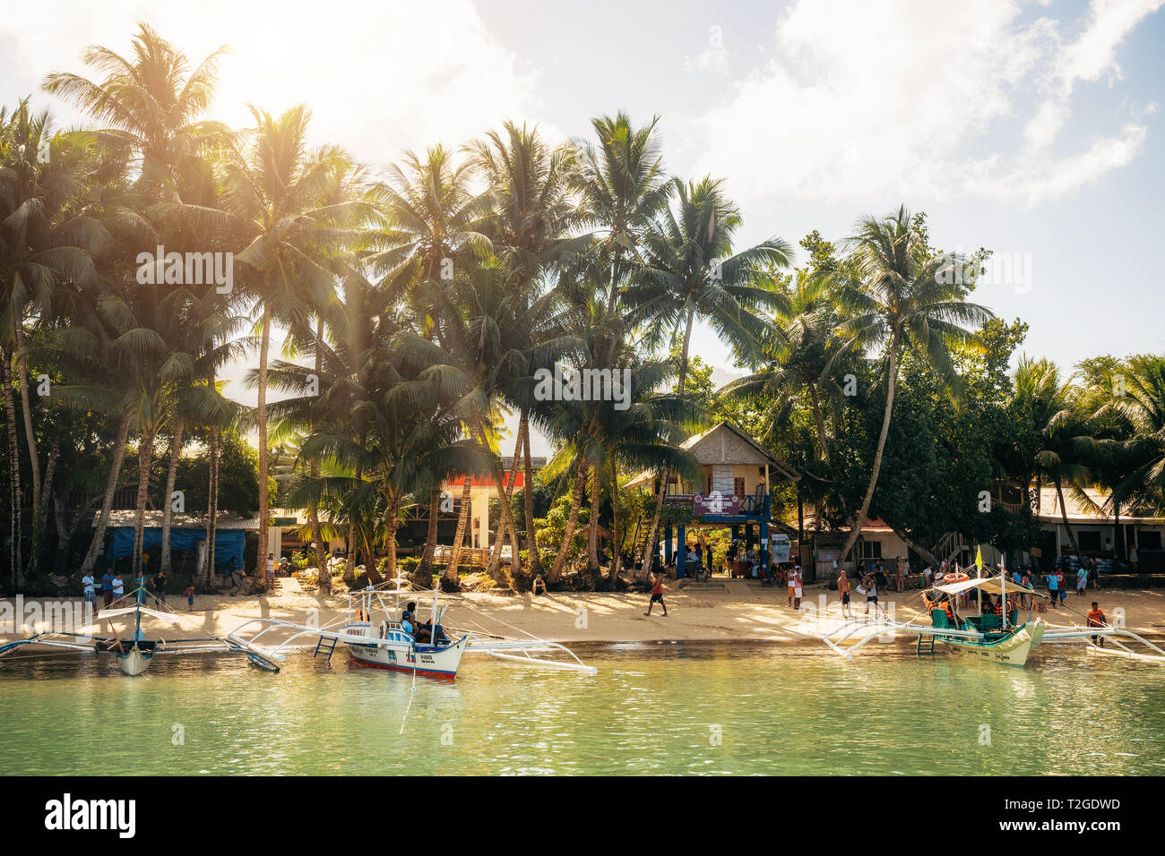 Port Barton, Palawan, Philippines - February 4, 2019: People on tropical beach with trees. Traditional boats in water Stock Photo
