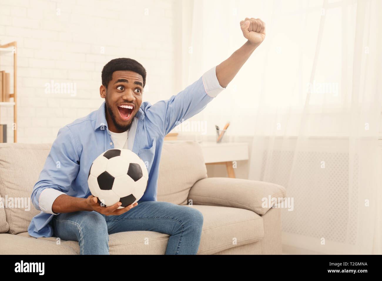 Emotional african american soccer fan watching sports on tv and