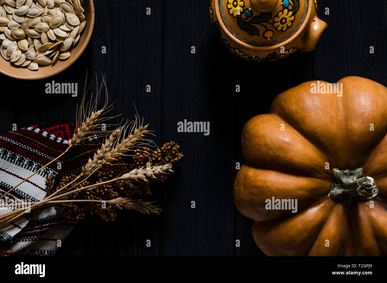 Orange pumpkin, pumpkin seeds and wheat ears lie on a black wooden background. top view Stock Photo