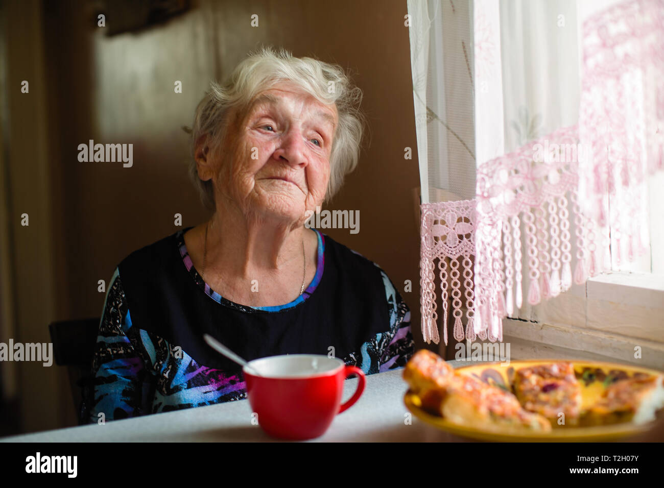 An elderly woman in the kitchen of his house sitting at the table Stock ...