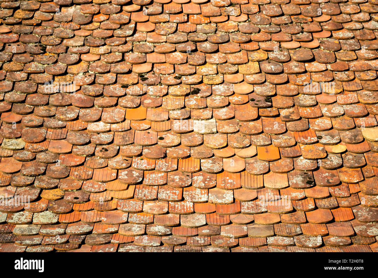 Abstract pattern of old, traditional, brown/orange, ceramic, overlapping shingles (tiles, schindle/schindel in German) on a house roof, lit in the mor Stock Photo
