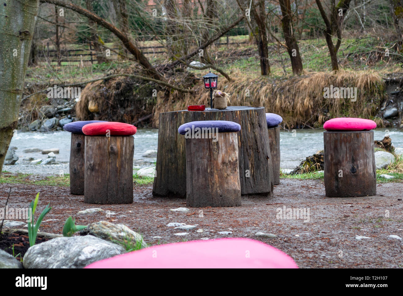 Table and chairs made from tree logs, with colorful cushions on each log/chair, near a river
