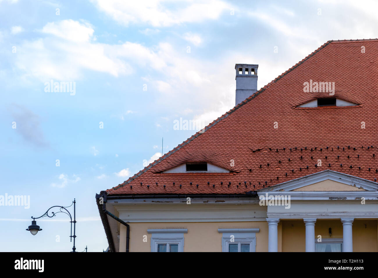 Traditional roof with small windows like eyes in Sibiu, Transylvania, Romania. Detailed architecture of a house top with columns, chimney, and a stree Stock Photo