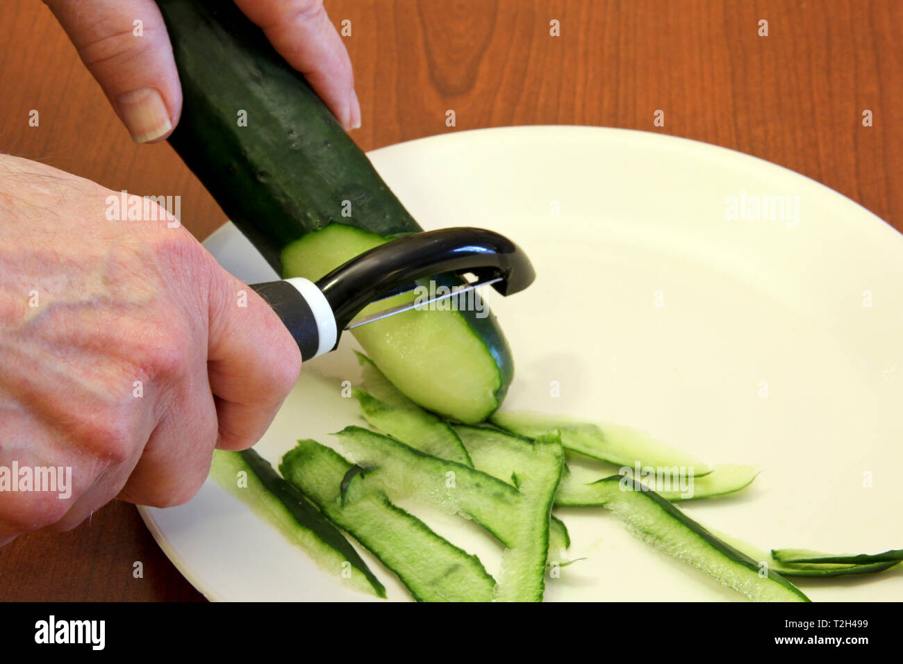 Chef peeling a Cucumber on a wooden cutting board Stock Photo