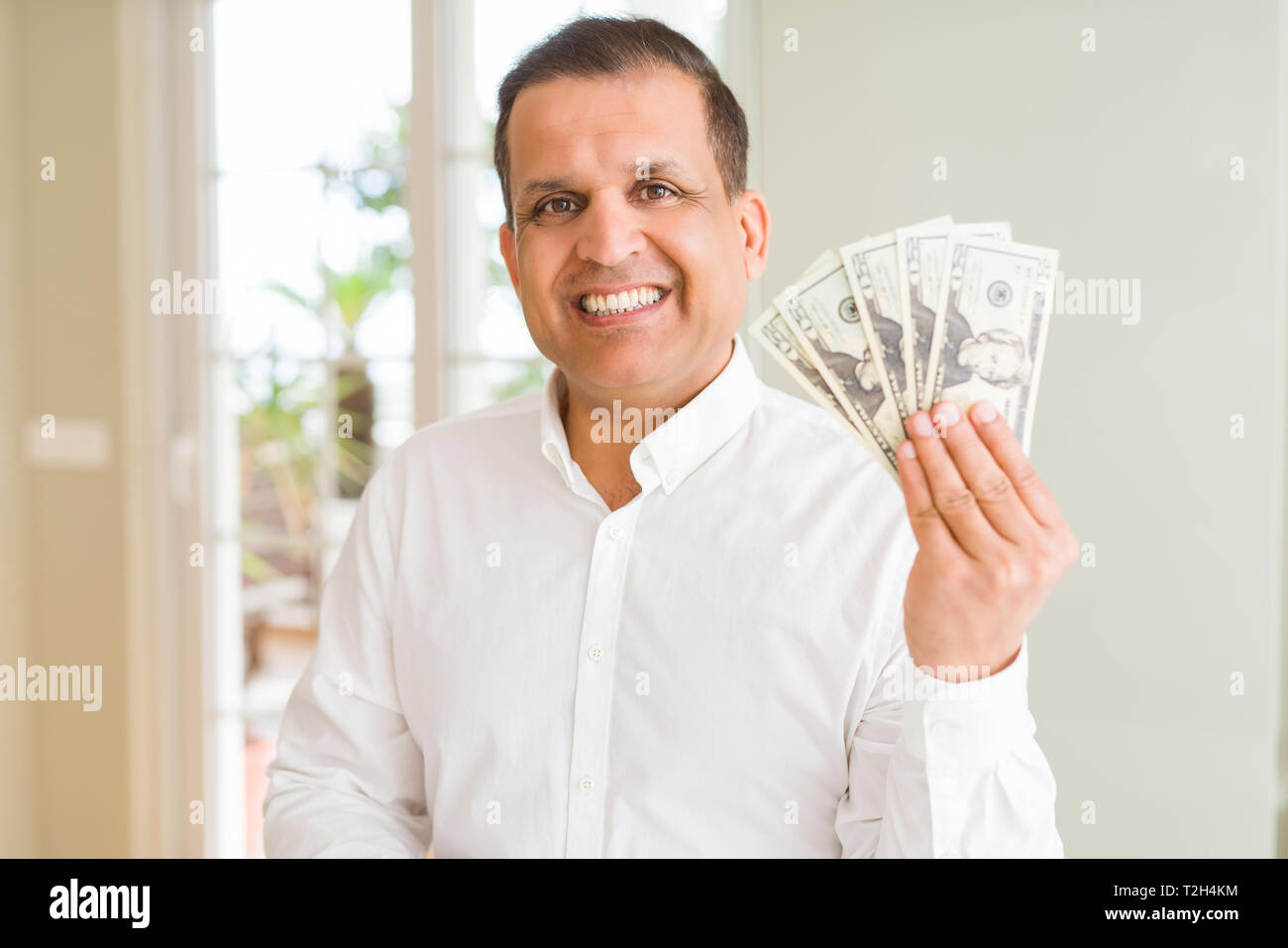 Middle age man holding bunch of dollars with a happy face standing and ...