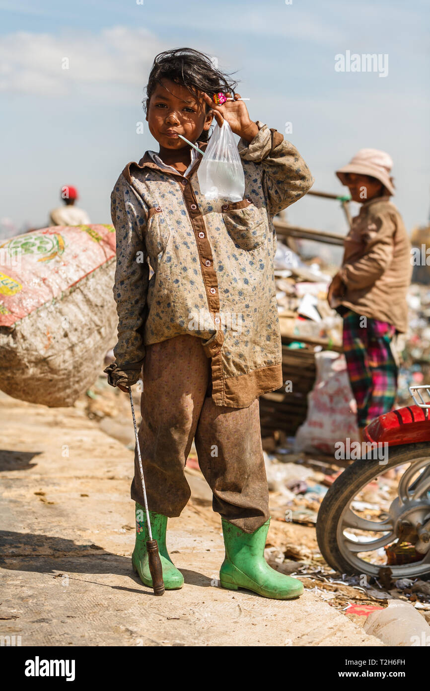 Child in green rubber boots drinking water while standing on edge of the Phenom Phen, Cambodia city dump. Stock Photo
