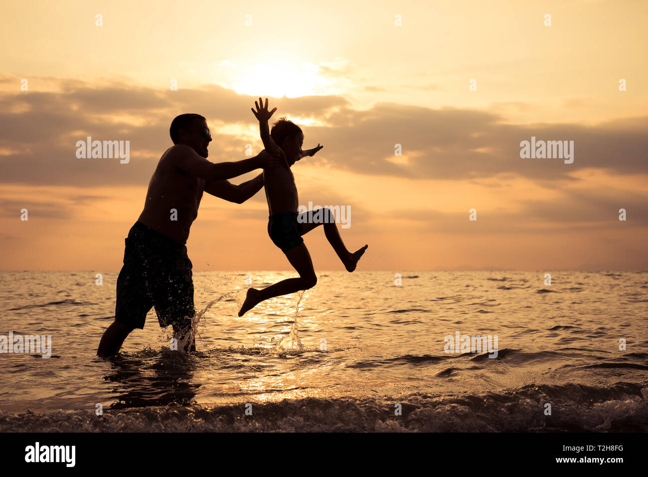 Father and baby son  playing on the beach at the sunset time. People having fun outdoors. Concept of summer vacation and friendly family. Stock Photo