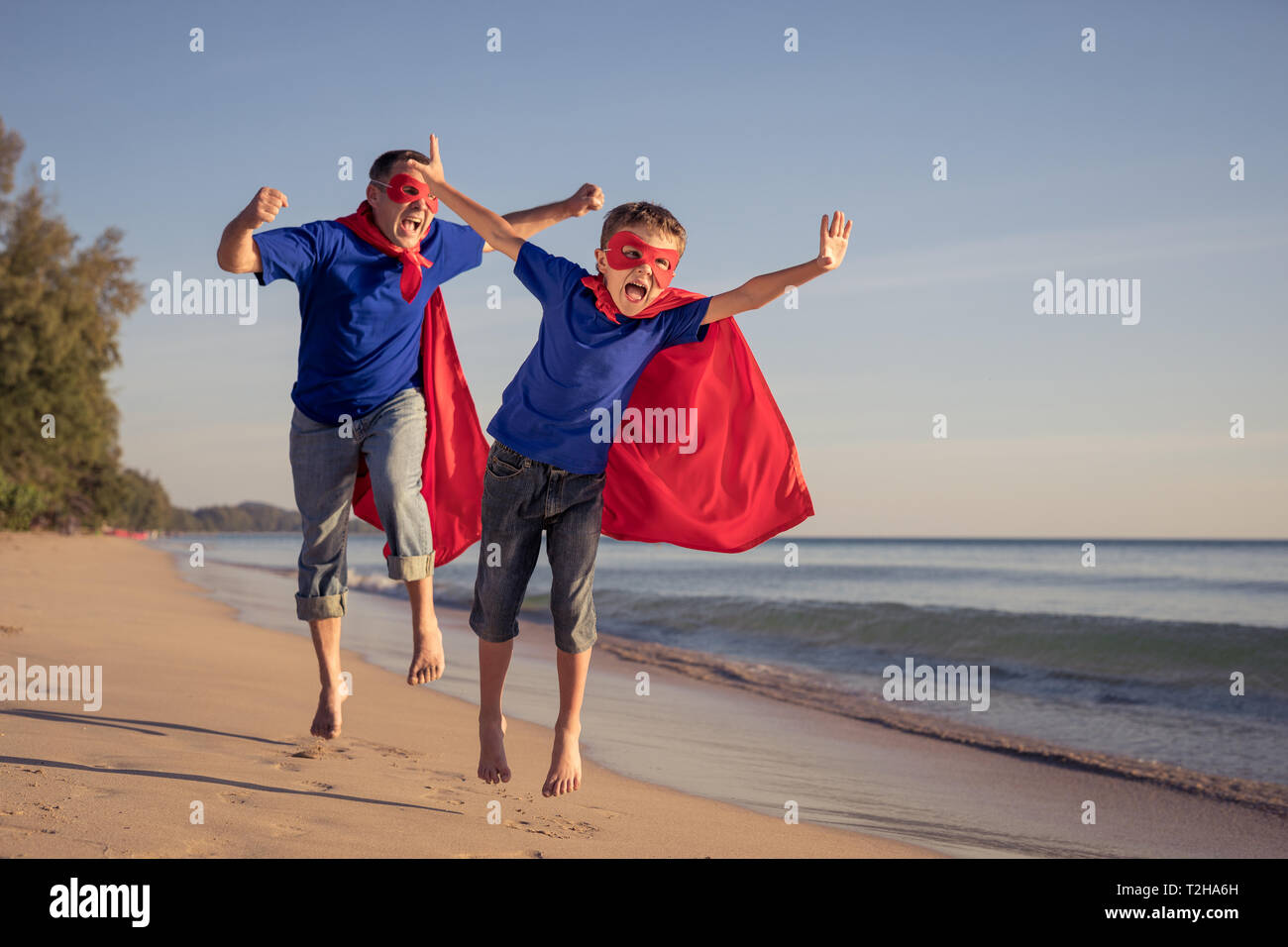 Father and son playing superhero on the beach at the day time. People having fun outdoors. Concept of summer vacation and friendly family. Stock Photo