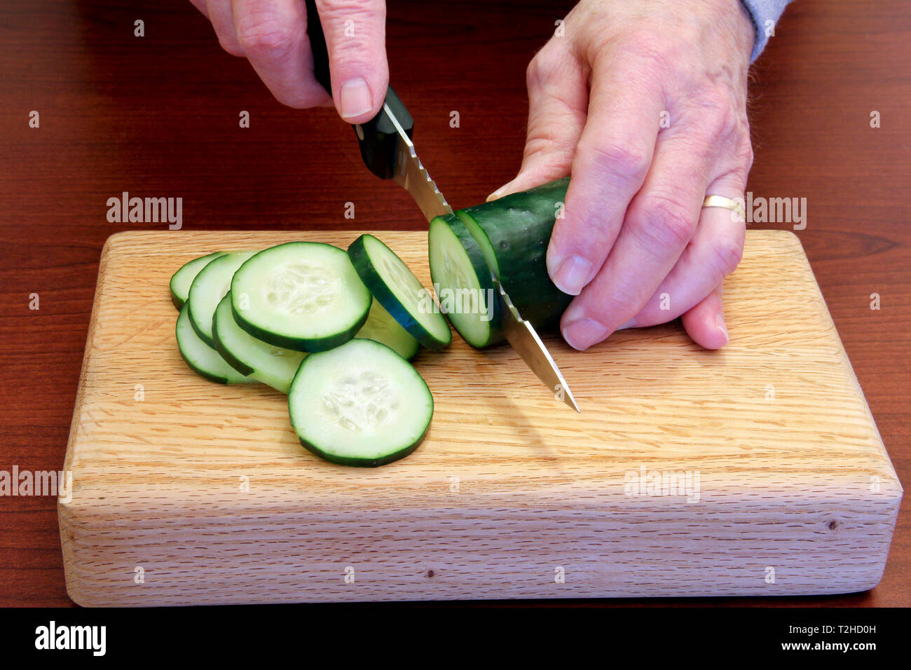 Chef slicing a Cucumber on a wooden cutting board Stock Photo
