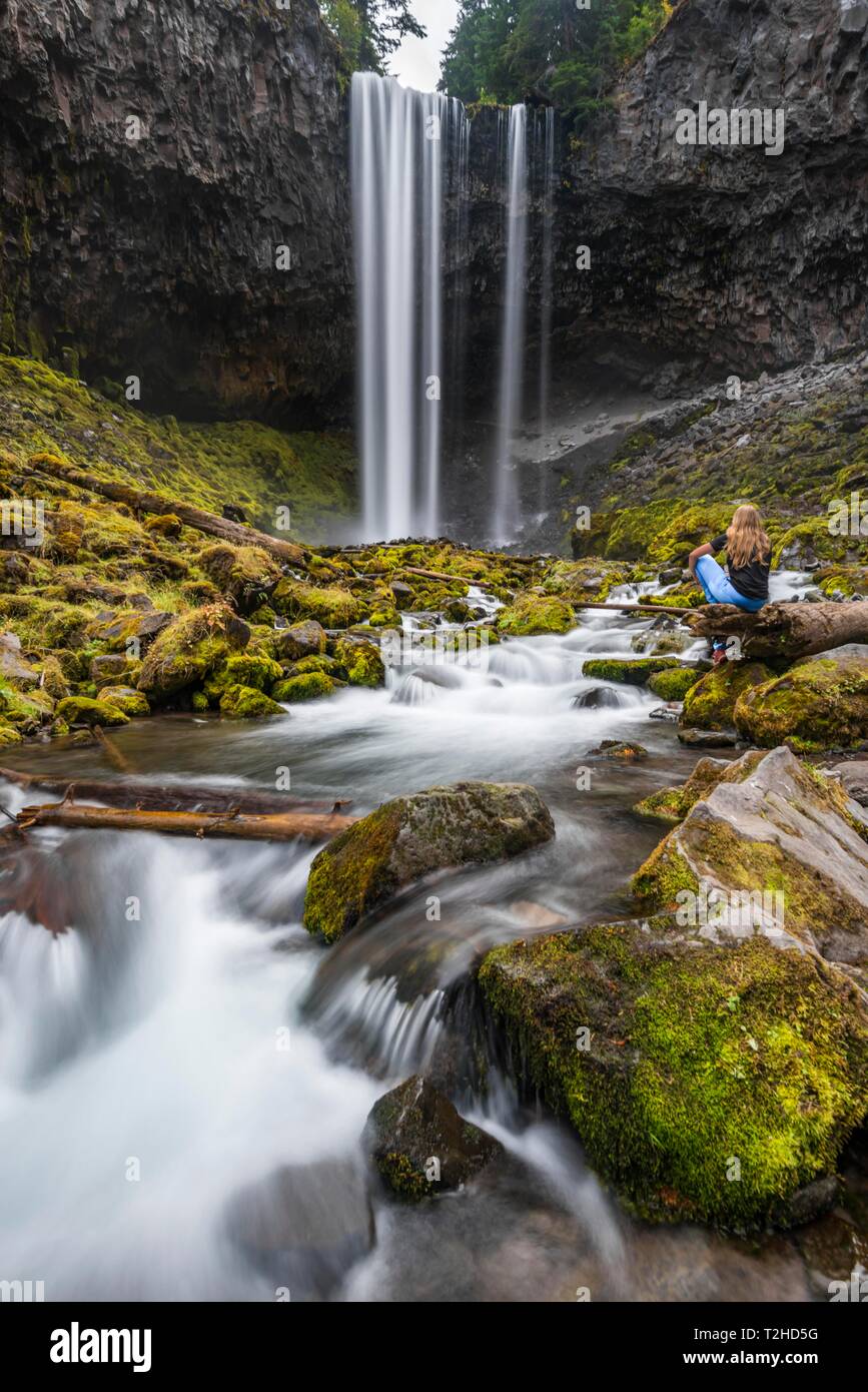 Young woman sitting at a river, hiker, waterfall plunging down a cliff, time exposure, river Cold Spring Creek, Tamanawas Falls, Oregon, USA Stock Photo