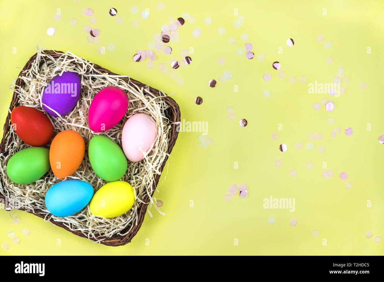 Colored Easter eggs in the basket on yellow background with confetti. Flat lay. Stock Photo