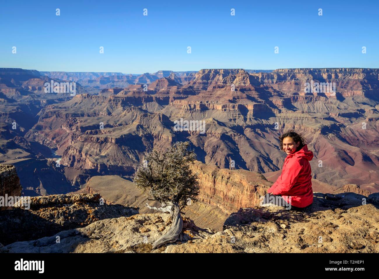 Young woman, tourist sitting at the edge of the gorge of the Grand Canyon, Colorado River, eroded rock landscape, South Rim, Grand Canyon National Stock Photo