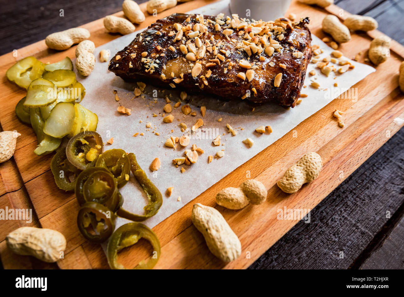 Closeup of pork ribs grilled with BBQ sauce served with peanuts and jalapeno. Selective focus Stock Photo