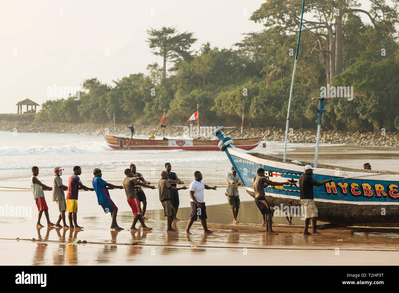 Men pulling boat out to sea, Busua, Ghana, Africa Stock Photo