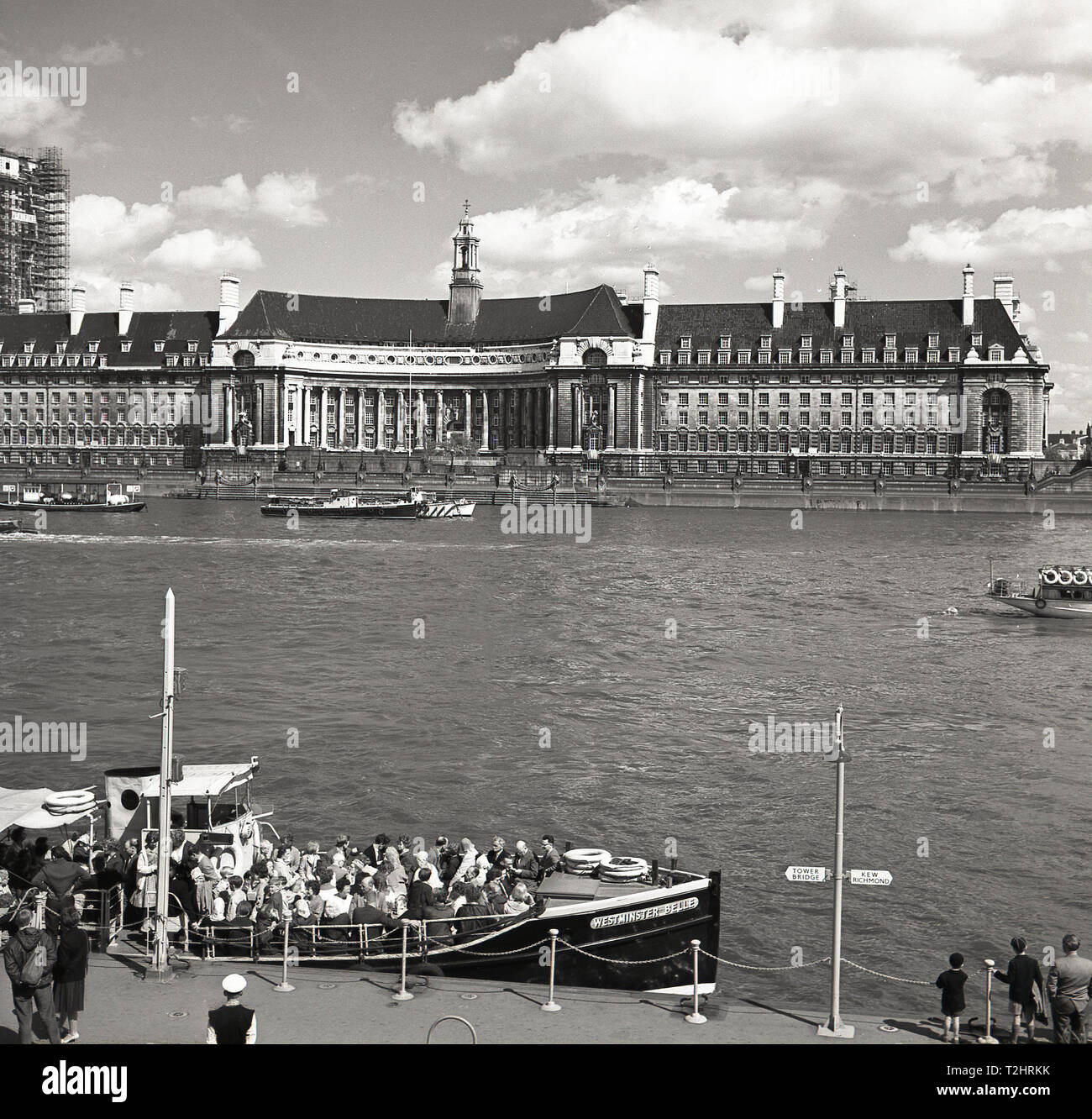 1960s, historical, picture shows Westminster Pier, with people crowded onto a tourist boat, 'Westminster Belle', London, England, UK, with County Hall, former home of the London County Council (LCC) the grand building sitting on the riverbank opposite. Stock Photo
