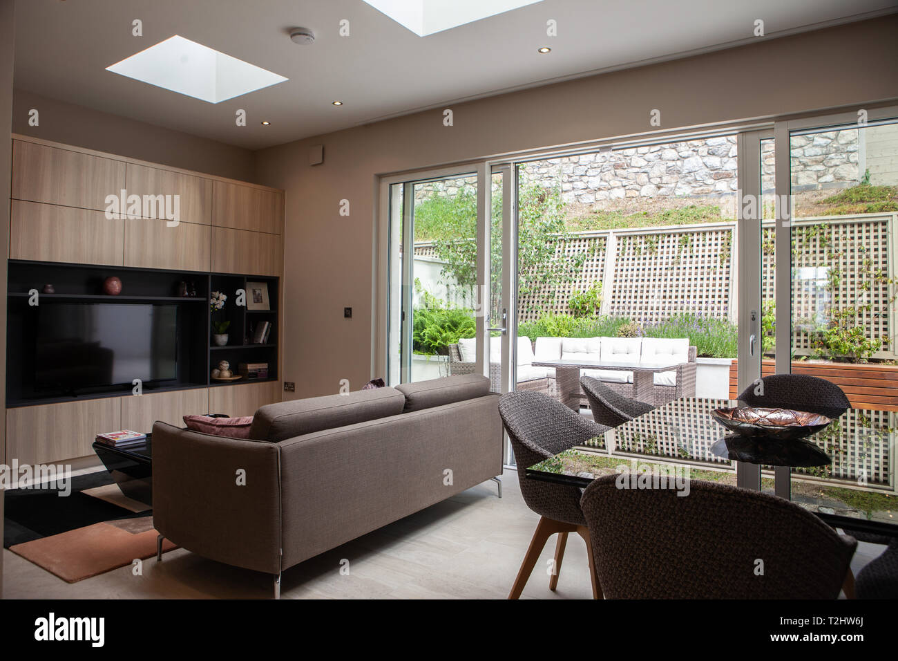 A modern family room and living space in the rear of a house featuring a couch, large TV and dining table area with patio doors and back garden. Stock Photo