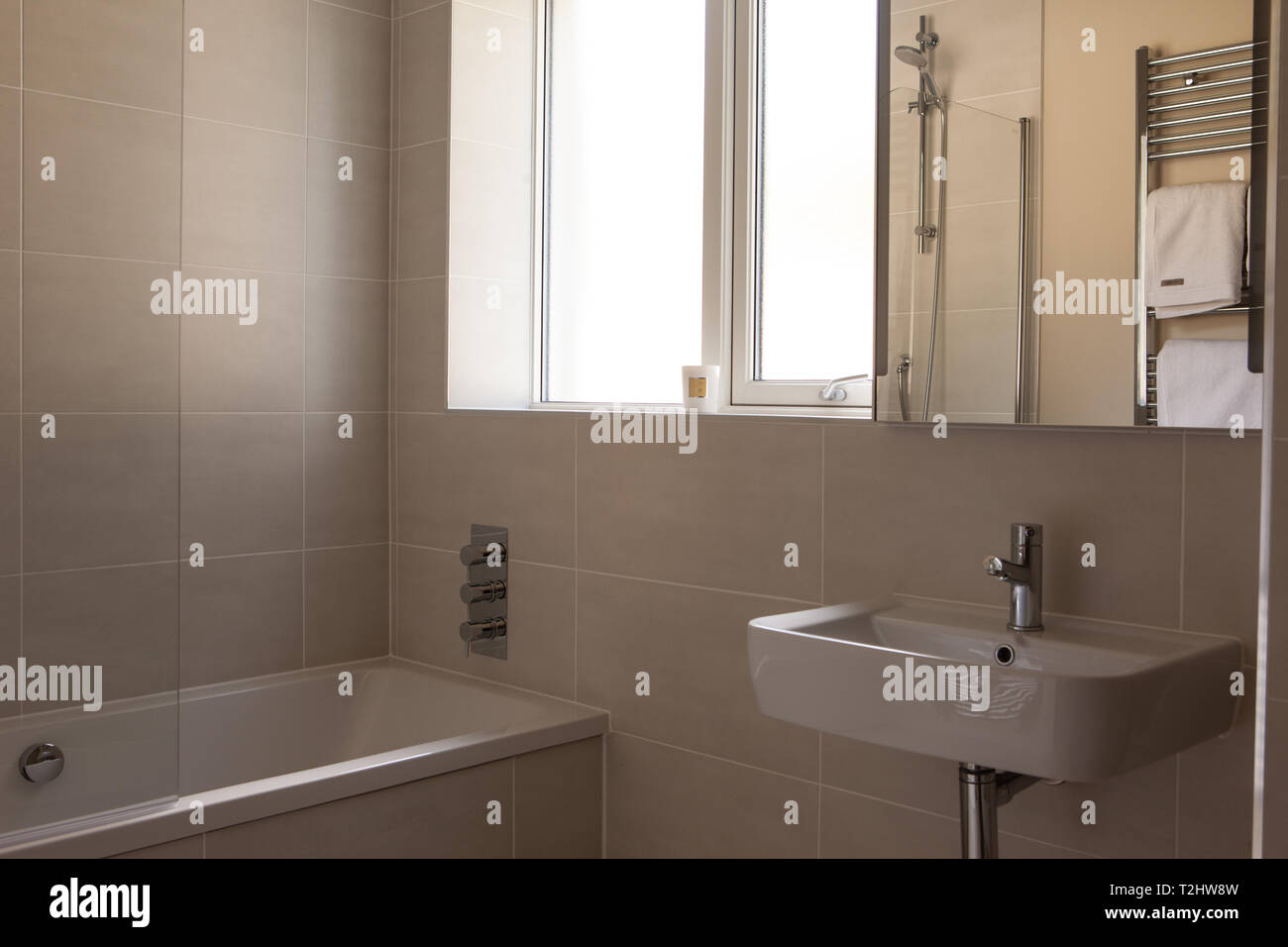 main bathroom with bath, sink and mirrored bathroom cabinet on the wall with bright light from window. Stock Photo