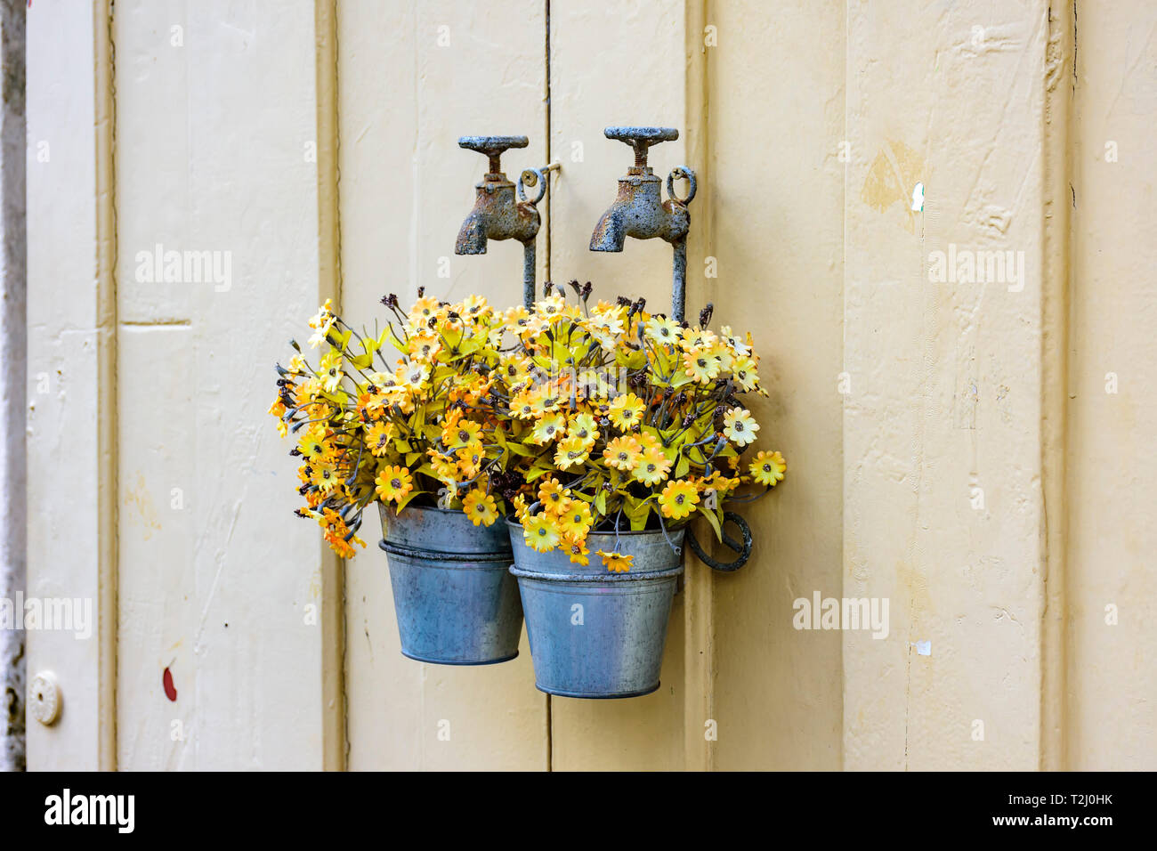 Bucket with yellow flowers hanging on an old metal faucet decorating a wooden door at the entrance of a house Stock Photo