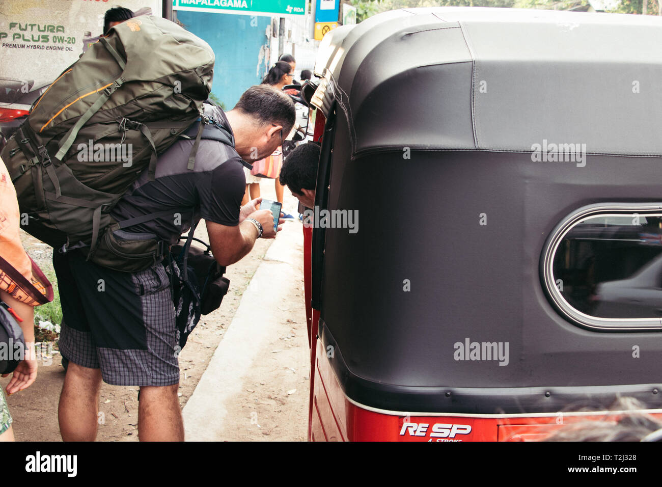 Galle, Sri Lanka - February 17th, 2019: A backpacker showing his mobile to a tuk tuk driver asking for directions at the sideroad of Matara  road in G Stock Photo