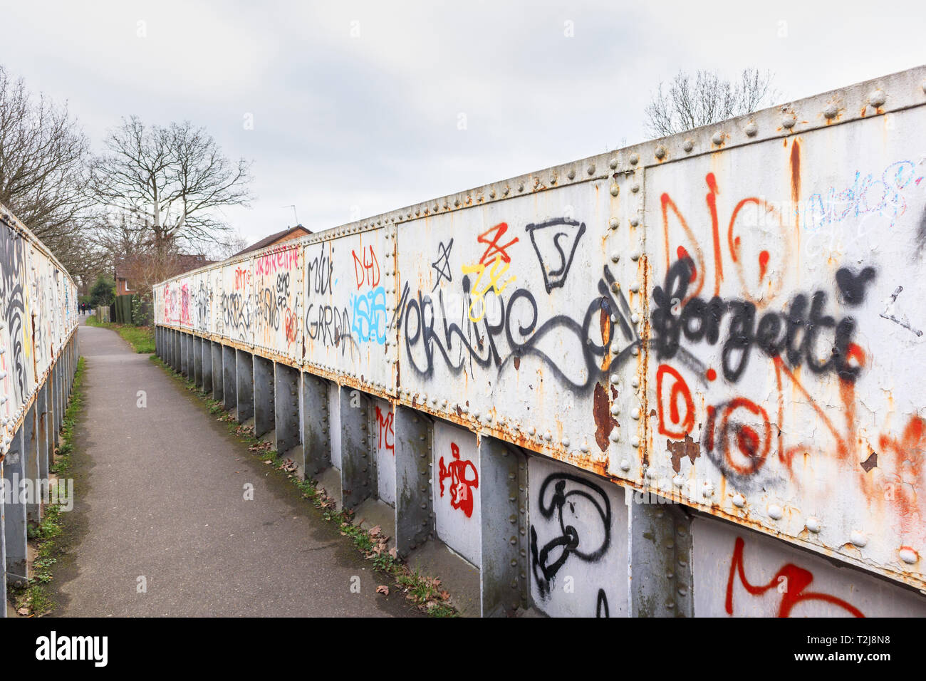 Spray paint grafitti on an old rusting iron railway footbridge on a footpath in Woking, Surrey, south-east England, UK Stock Photo