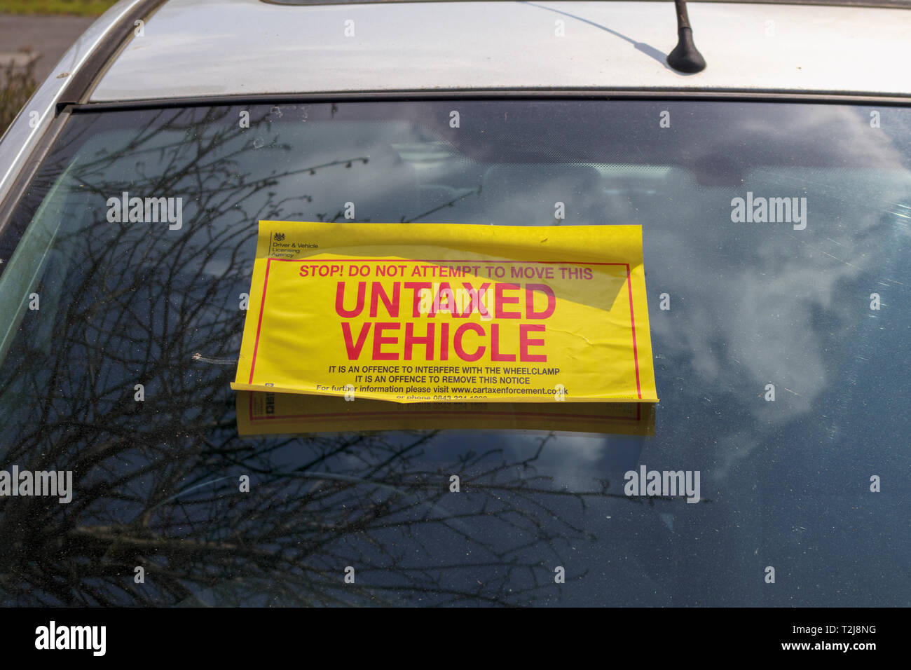 Untaxed vehicle sticker on the windscreen of a car immobilised at the roadside by a yellow DVLA clamp, for non-payment of road tax Stock Photo