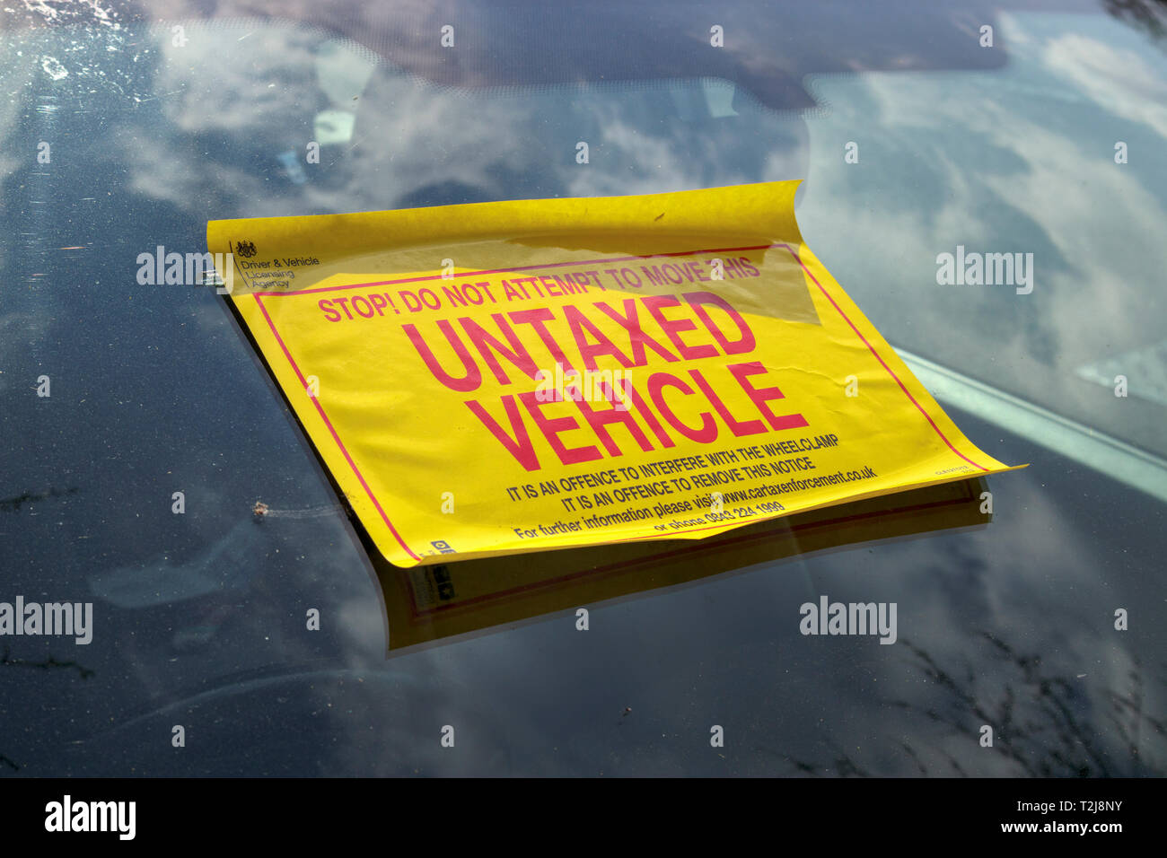 Untaxed vehicle sticker on the windscreen of a car immobilised at the roadside by a yellow DVLA clamp, for non-payment of road tax Stock Photo