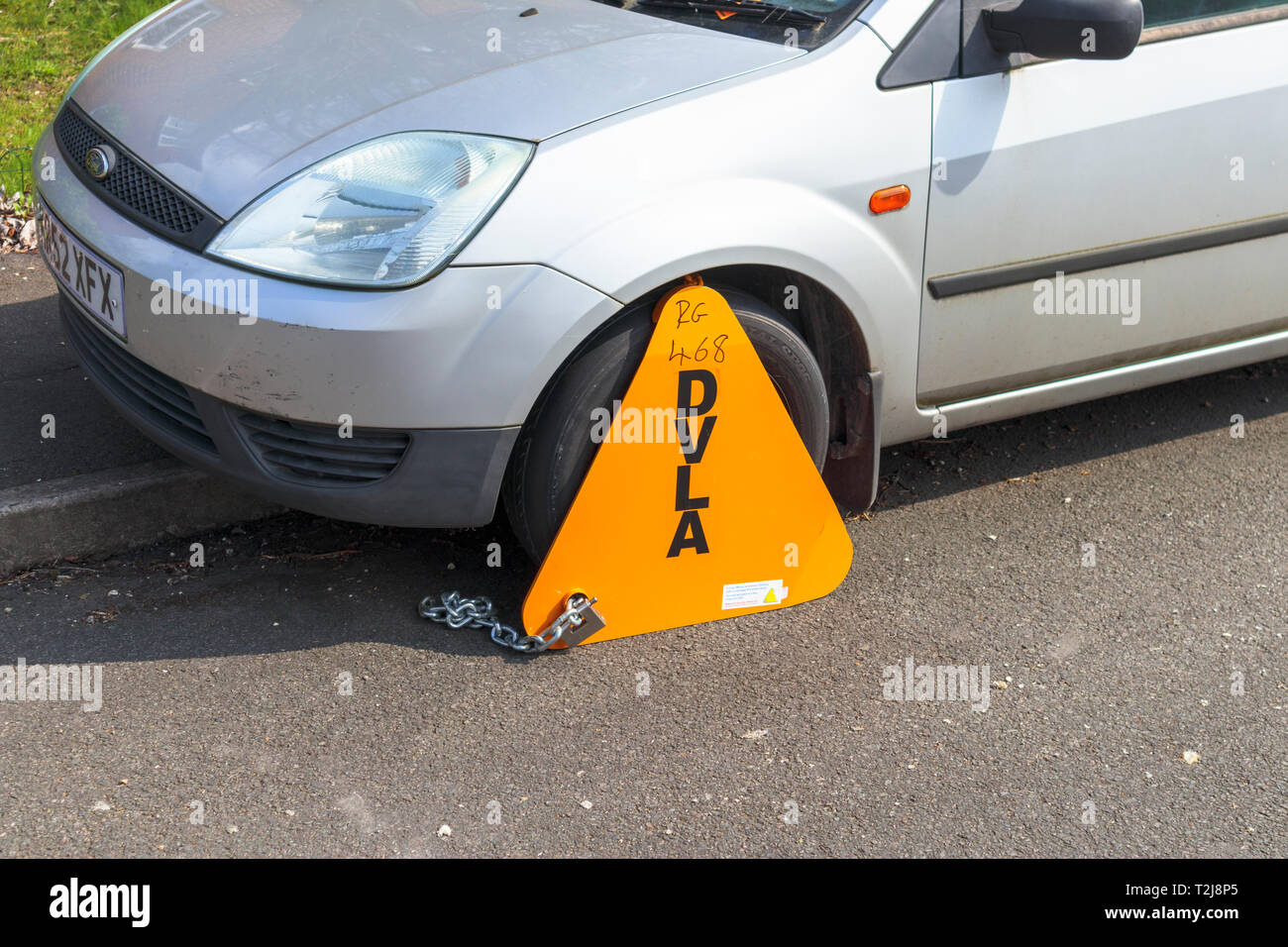 Untaxed vehicle immobilised at the roadside by a yellow DVLA clamp, for nonpayment of road tax