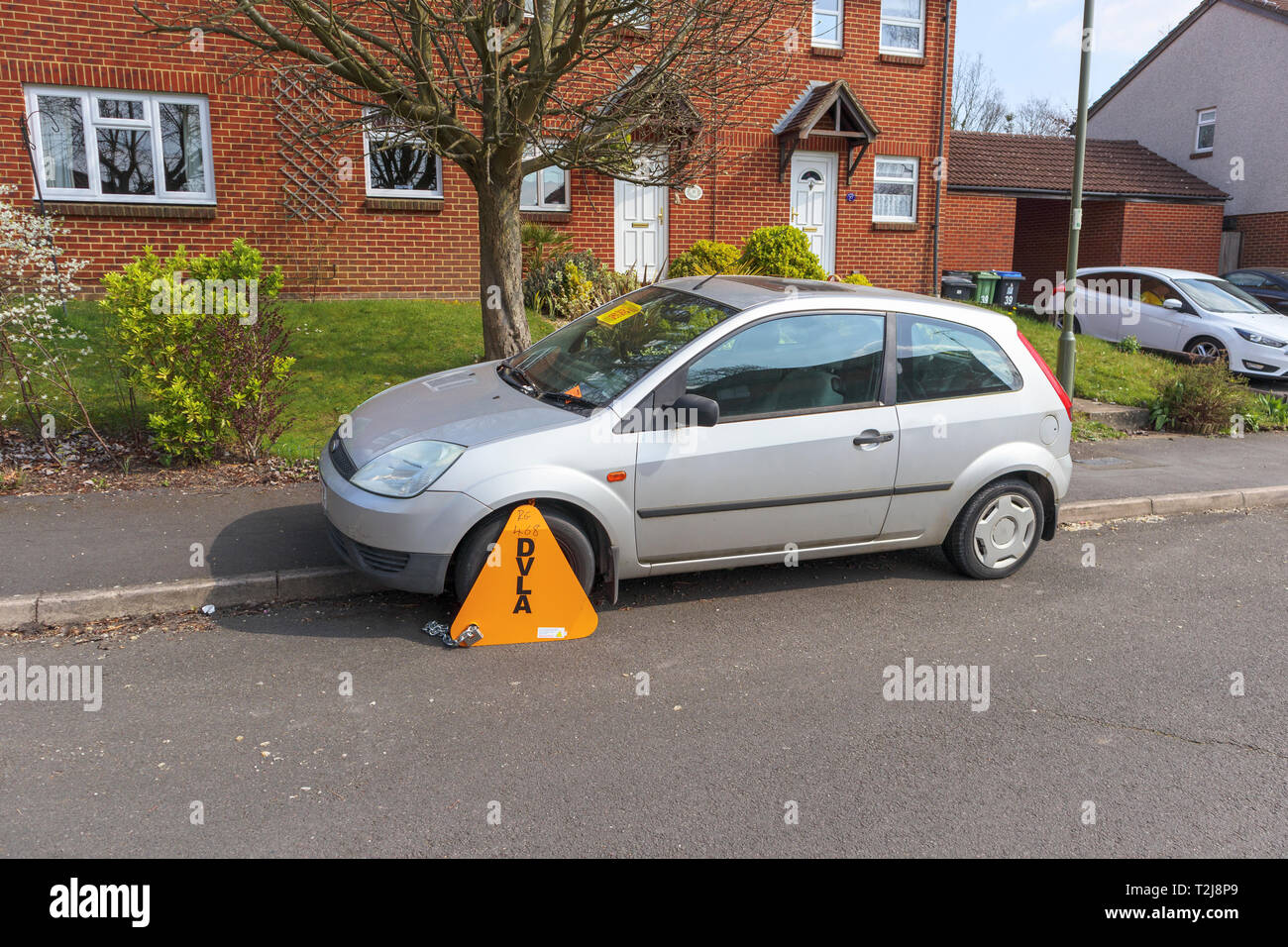 Untaxed car immobilised at the roadside by a yellow DVLA wheelclamp with sticker on the windscreen of non-payment of road tax Stock Photo