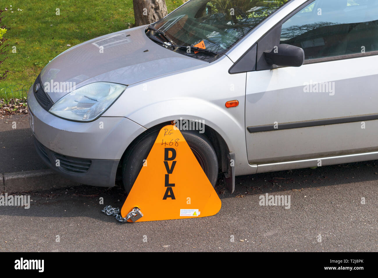 Untaxed vehicle immobilised at the roadside by a yellow DVLA clamp, for nonpayment of road tax