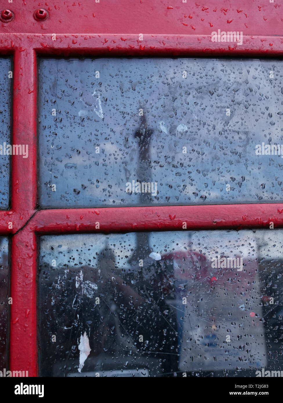 Raindrops on the outside of red London telephone box which reflects Nelson Column on Trafalgar Square on one of the changeable London weather days. Stock Photo