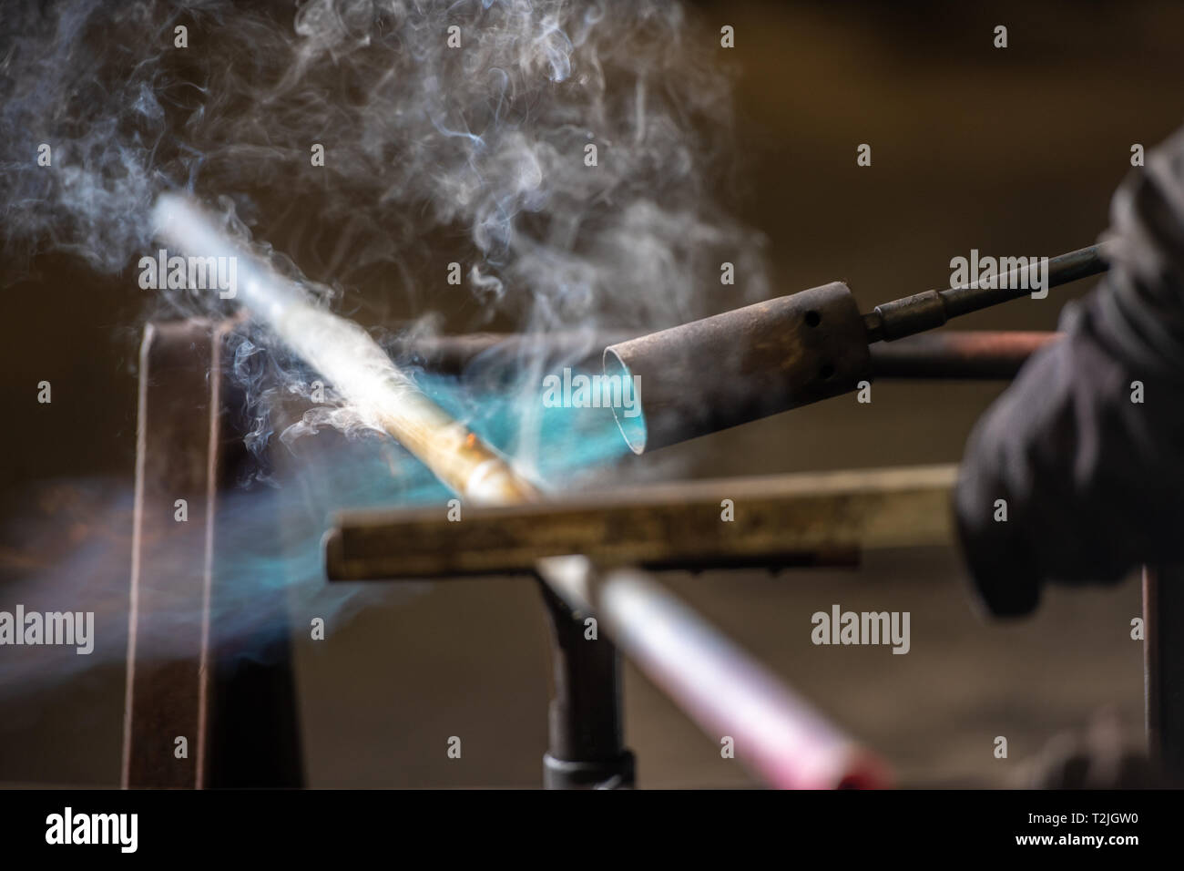 Light blowtorch blasts copper tube with hot blue flame to anneal it at