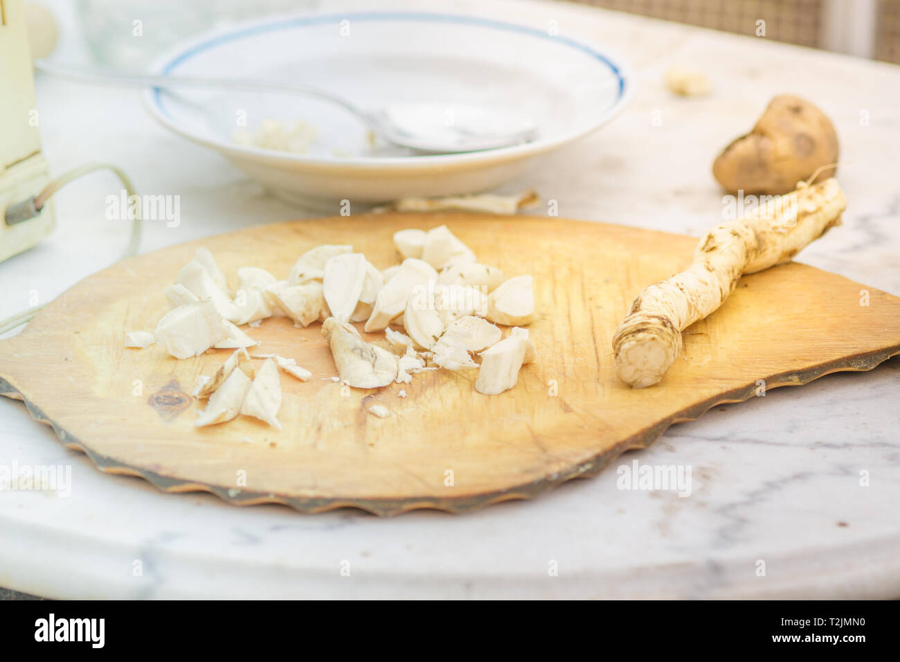 Horseradish root sliced on the board. Table with a plate. Stock Photo