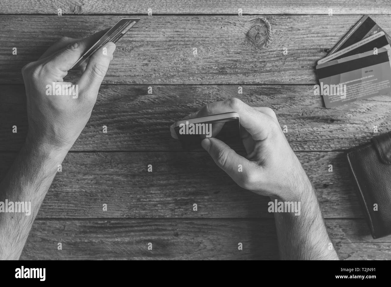 Man Hands holding credit card and using mobile phone. Online shopping, online banking and online marketing. top view,  black and white toning photo Stock Photo