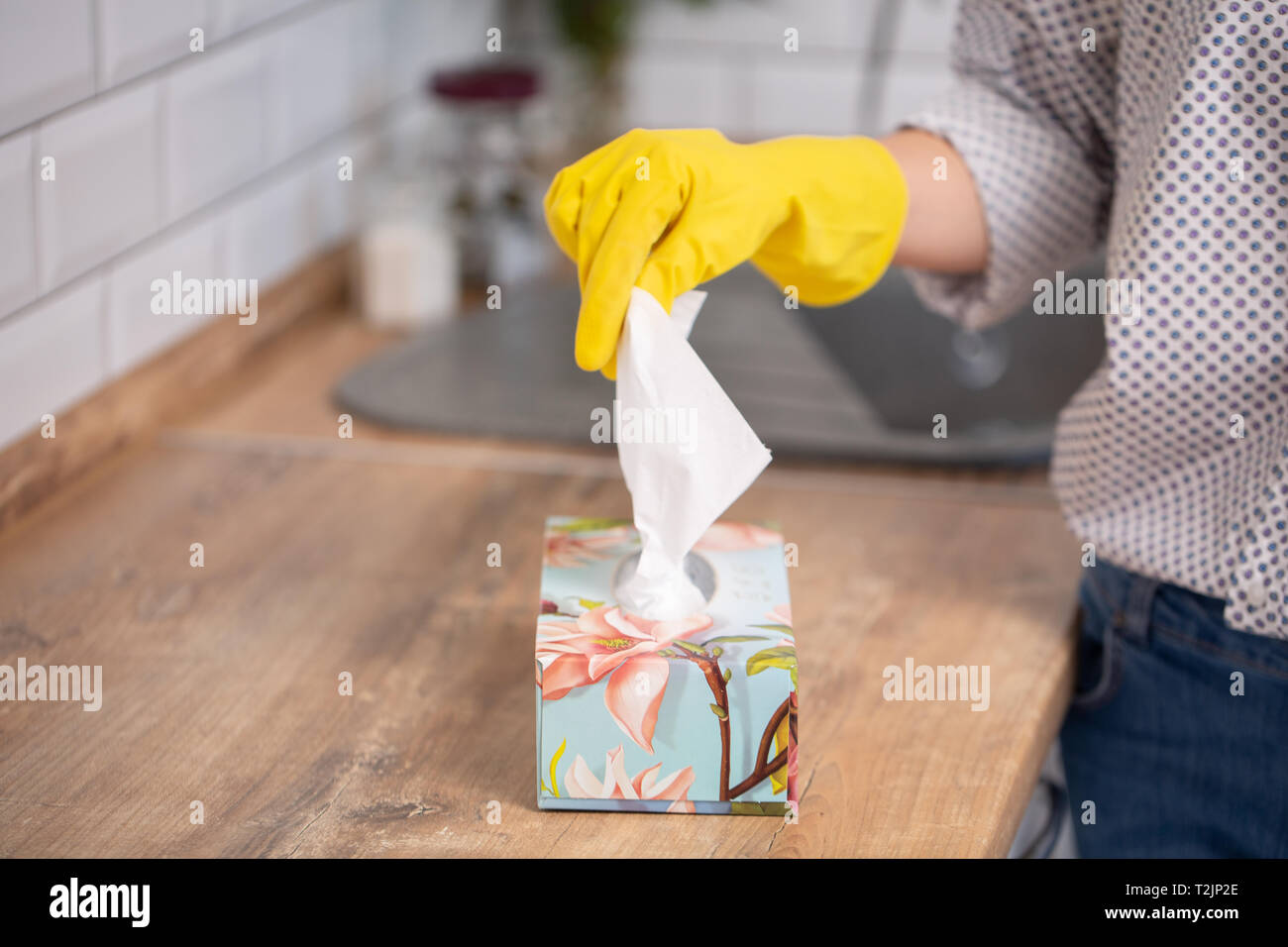 Woman taking paper tissue from napkin holder on table. Closeup photo of picking sanitary napkin out box. Hands wearing at rubber gloves Stock Photo